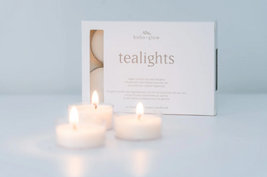 Three lit tealight candles in front of a white box of